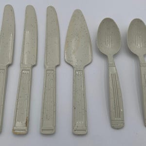 May include: Set of six white plastic utensils with a speckled pattern. The set includes three knives, a serving knife, and two spoons.