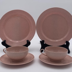 May include: A set of four pink speckled ceramic teacups and saucers. The cups and saucers have a simple, elegant design.