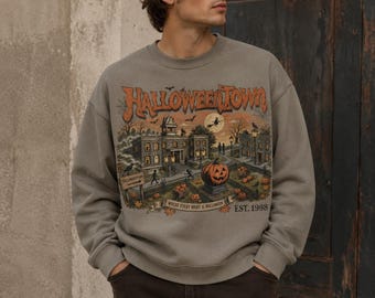 May include: A taupe crewneck sweatshirt featuring a graphic print of a spooky town scene with the text HALLOWEENTOWN, WHERE EVERY NIGHT IS HALLOWEEN, and EST. 1998. The illustration includes a large pumpkin, a witch on a broom, and buildings.