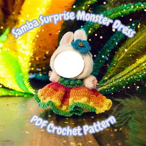 May include: A plush bunny doll wearing a colorful crochet dress with a blue flower. The text "Samba Surprise Monster Dress" and "PDF Crochet Pattern" are displayed on the image. The dress features shades of orange, yellow, and green.