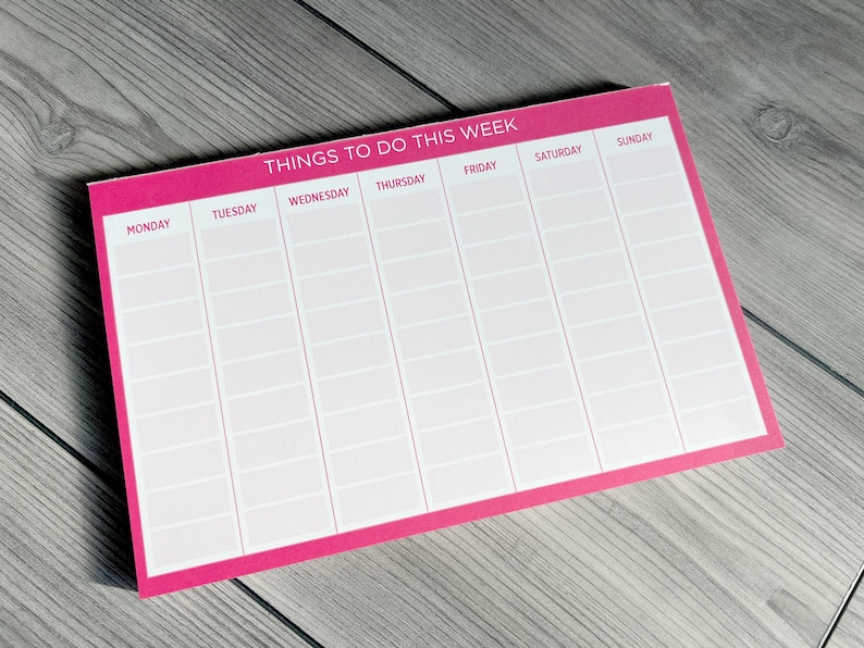 A pink weekly planner notepad with white text. The top of the notepad says 'Things To Do This Week.'  Each day of the week is listed across the top: Monday, Tuesday, Wednesday, Thursday, Friday, Saturday, Sunday.  Rows of blank spaces are provided under each day for writing tasks or appointments. The notepad is a useful tool for organizing and scheduling weekly activities.