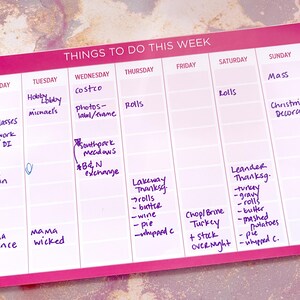 A pink weekly planner with daily sections for scheduling tasks.  The planner includes handwritten entries for various errands, appointments, and Thanksgiving preparations, such as grocery shopping, cooking, and decorating.  The text 'Things To Do This Week' is at the top.  Days of the week are listed across the top, from Monday to Sunday.  Specific tasks include: HEB, Sally glasses, Hobby Lobby, Michael's, Costco, photos-label/frame, rolls, Mass, Christmas decorating, Thanksgiving, and more.
