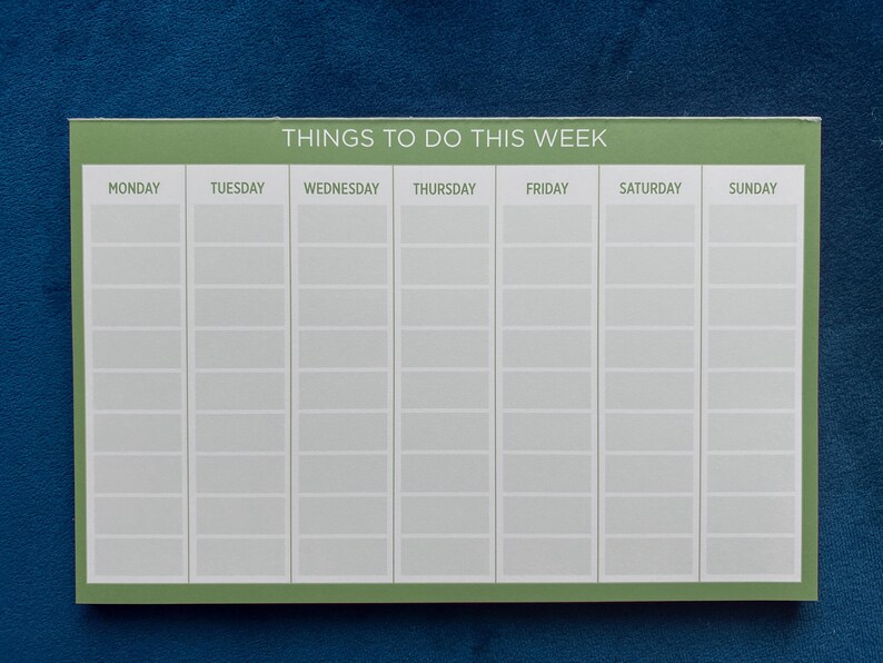 A weekly planner notepad with a sage green border. The days of the week are listed across the top: Monday, Tuesday, Wednesday, Thursday, Friday, Saturday, Sunday.  Each day has multiple blank lines for writing tasks or appointments. The title at the top reads: 'Things To Do This Week'.