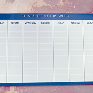 A weekly planner notepad with a dark blue border. The days of the week are listed across the top: Monday, Tuesday, Wednesday, Thursday, Friday, Saturday, Sunday.  Each day has multiple blank lines for writing tasks or appointments. The title at the top reads: 'Things To Do This Week'.