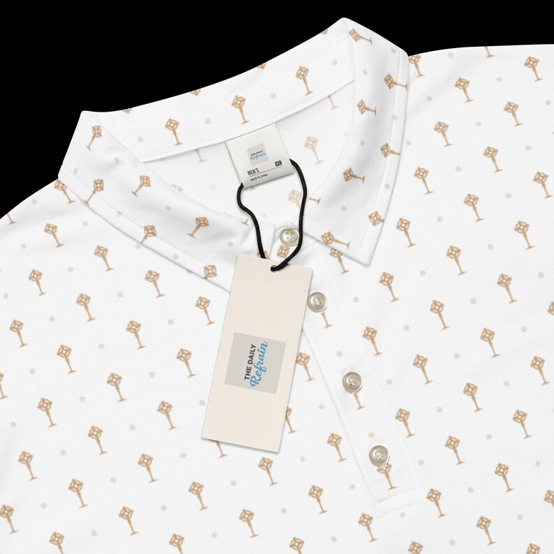 Op de afbeelding: Witte poloshirt met een herhalend goudkleurig sleutelpatroon en kleine stippen. De blouse heeft een kraag, drie knopen en een label met "The Daily Refrain".