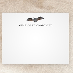 May include: A white card with a bat illustration and the text "CHARLOTTE WOODSBURY" printed in black.