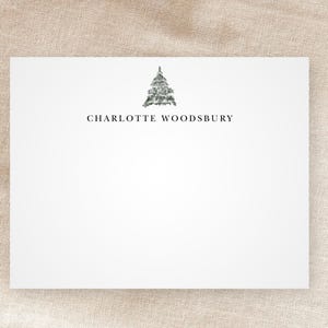 May include: A white card with a simple black and gray pine tree illustration and the text "CHARLOTTE WOODSBURY" printed in black.