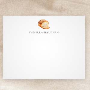 May include: White stationery card with a simple design featuring a loaf of bread and the text "CAMILIA BALDWIN".