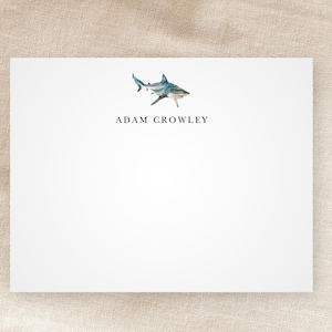 May include: A white card with a watercolor illustration of a shark and the text "ADAM CROWLEY" printed in black.