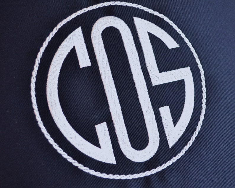 May include: A navy blue fabric with a white embroidered monogram of the letters "COS" in a circle.