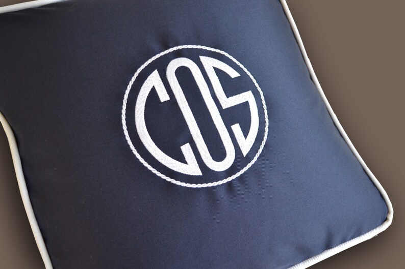 May include: A navy blue pillow with a white monogram of the letters "COS" in a circle. The pillow has a white piping around the edge.