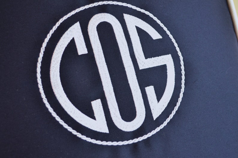 May include: A navy blue fabric with a white embroidered circle containing the letters "COS" in a monogram style.
