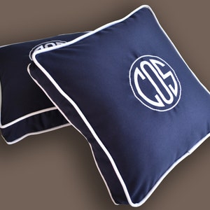 May include: Two navy blue square throw pillows with white piping and a white monogram "COS" on one pillow.