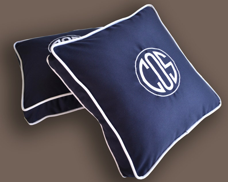 May include: Two navy blue square throw pillows with white piping and a white monogram "COS" on one pillow.