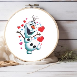 Può includere: Uno schema di punto croce con Olaf, il pupazzo di neve del film Frozen, circondato da cuori rossi e blu.