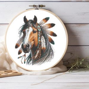 Pode incluir: Um padrão de ponto cruz de um cavalo usando uma cobertura de cabeça com penas. O cavalo é marrom e branco com uma juba e cauda pretas. A cobertura de cabeça é azul, verde e marrom.
