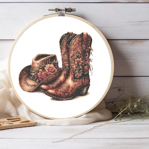 Puede incluir: Un par de botas de vaquero marrones con bordados florales y un sombrero de vaquero marrón con detalles florales.