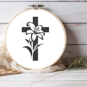 Pode incluir: Cruz preta e branca com uma flor de lírio na frente. A cruz e a flor estão sobre um fundo branco.
