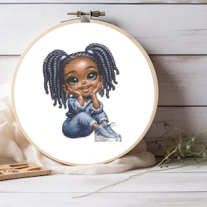 Peut inclure: Un motif de point de croix dans un tambour à broder circulaire en bois représentant un personnage de dessin animé à la peau foncée avec des cheveux bleus tressés en couettes. Le personnage porte une tenue en jean bleu et des baskets bleues.