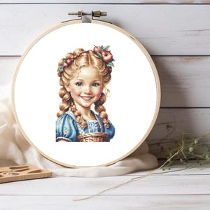 Op de afbeelding: Een kruissteekpatroon van een jong meisje met blonde vlechten, die een blauwe jurk draagt en een mand met appels vasthoudt. Het meisje glimlacht en heeft een bloemenkrans op haar hoofd.