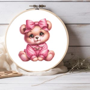 Puede incluir: Un oso de peluche rosa que lleva un vestido rosa con un lazo rosa en la cabeza. El oso tiene ojos marrones y una nariz marrón.