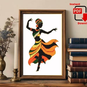 May include: A framed cross-stitch pattern featuring a silhouette of a dancer in a flowing skirt. The dancer wears a headpiece and jewelry in shades of orange, green, yellow, and black. The text Instant PDF Download is visible in the upper right corner.