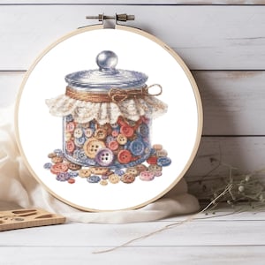 Puede incluir: Bordado de punto de cruz de un tarro de cristal lleno de botones de colores. El tarro tiene una tapa plateada y está decorado con encaje beige y cuerda. El bordado está en un bastidor de madera.