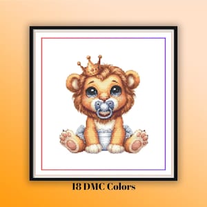 Può includere: Un motivo a punto croce incorniciato con un cucciolo di leone dei cartoni animati con una corona d'oro e un ciuccio. Il cucciolo di leone è seduto e indossa un pannolino. Il testo "18 DMC Colors" è nella parte inferiore della cornice.