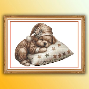 May include: A cross-stitch pattern featuring a brown puppy wearing a matching nightcap and pajamas, sleeping peacefully on a white pillow decorated with small brown and green stars. The entire design is enclosed within a rectangular wooden frame.