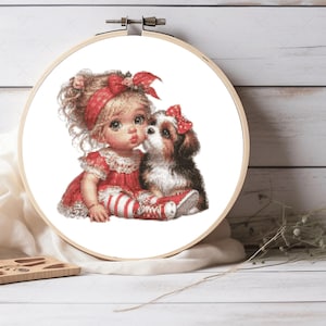 Puede incluir: Un bastidor de bordado circular de madera que contiene un patrón de punto de cruz de un niño pequeño de cabello rubio con un vestido rojo y una diadema roja, sentado junto a un perro pequeño marrón y blanco con un lazo rojo en la cabeza.
