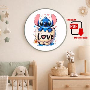 May include: A round framed print featuring a blue cartoon character emerging from a cracked egg. The egg has the word "LOVE" on it. The print is surrounded by a white border and the background is a light beige.