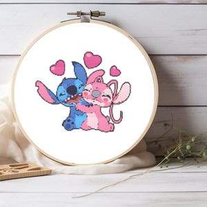 Puede incluir: Patrón de punto de cruz bordado con Stitch y Angel de Lilo & Stitch, abrazándose con corazones a su alrededor.