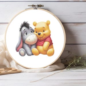 Pode incluir: Um padrão de ponto cruz com o Ursinho Pooh e o Burrico, dois personagens queridos da franquia Disney. O padrão mostra os dois personagens sentados juntos, com o Ursinho Pooh vestindo uma camisa vermelha e o Burrico com uma aparência triste.