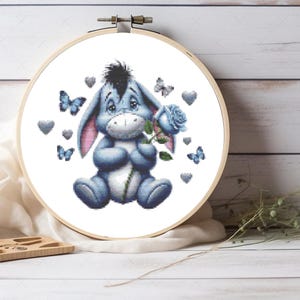 May include: A blue donkey holding a blue rose with a green stem. The donkey is surrounded by blue butterflies and gray hearts. The image is on a white background.
