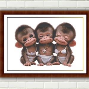 May include: A cross-stitch pattern featuring three brown baby monkeys sitting side-by-side. The monkeys have dark brown fur, pinkish ears, and are wearing white diapers. The center monkey wears a necklace, while the others wear white tops.