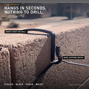 Può includere: Un gancio da parete nero Zion Forged con una tacca di fissaggio per cavi, progettato per essere appeso sopra un muro. Testo: ZION FORGED, HANGS IN SECONDS. NOTHING TO DRILL., DROPS OVER THE WALL, WIRE CAPTURE NOTCH, STUCCO, BLOCK, FENCE, BRICK, 2026 Zion Forged LLC.