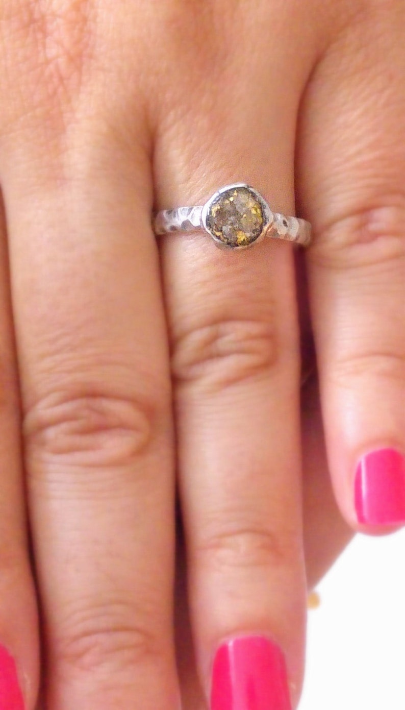 K&ouml;nnte beinhalten: Ein silberner Ring mit einem geh&auml;mmerten Band und einem runden, gefassten, braunen und goldenen Edelstein.
