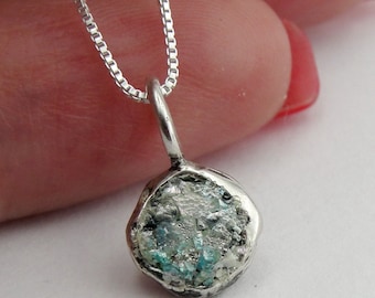 May include: A silver chain necklace with a pendant featuring a round piece of ancient Roman glass, also known as Roman glass, with a blue and green color scheme.