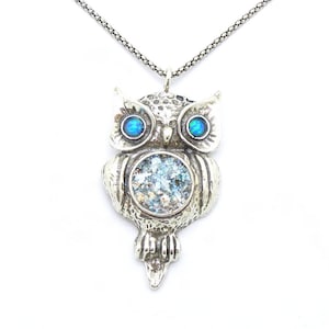 Könnte beinhalten: Silberne Eulen-Anhänger-Kette mit blauen Opalaugen und einem runden, klaren, schillernden Glaszentrum. Die Kette hat eine silberne Kette.