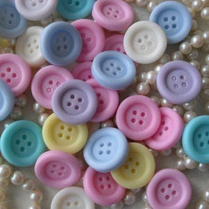 May include: Assortment of pastel colored buttons with a pearl necklace in the background. The buttons are various shades of pink, blue, yellow, and purple.