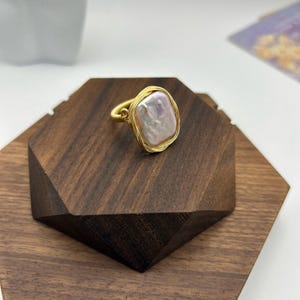 May include: A gold wire wrapped ring featuring a large, off-white baroque pearl.