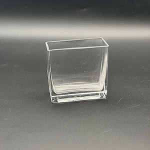 May include: A clear glass vase with a rectangular shape and a flat base. The vessel features smooth, transparent walls and an open top, showcasing a simple, functional design constructed from solid, colorless glass material throughout.