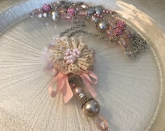 May include: A delicate pink and cream necklace with a flower charm and a pearl drop. The necklace features a silver chain and pink and cream beads.
