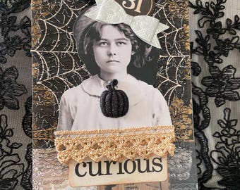 May include: A handmade Halloween-themed card featuring a vintage photograph of a girl wearing a bow. The card has a black and gold spiderweb design, a gold lace trim, and a black glitter pumpkin. The word "curious" is printed on the card.