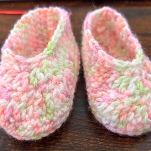 Op de afbeelding: Een paar gehaakte babyschoentjes in roze, wit en groen.