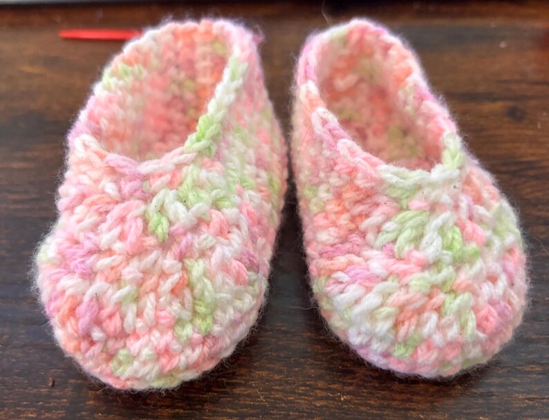 Op de afbeelding: Een paar gehaakte babyschoentjes in roze, wit en groen.