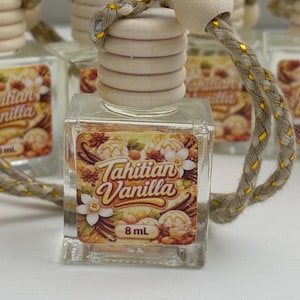 Puede incluir: Botella de ambientador para coche de cristal transparente con tapón de madera y cuerda trenzada. La etiqueta dice "Tahitian Vanilla" con ilustraciones florales y de especias. Contiene 8 ml de fragancia.