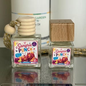 May include: Two clear glass square bottles labeled Sangria Punch, each containing liquid and topped with a wooden cap. The left bottle features a hanging cord with a wooden bead, while the right bottle has a simple square wooden lid.