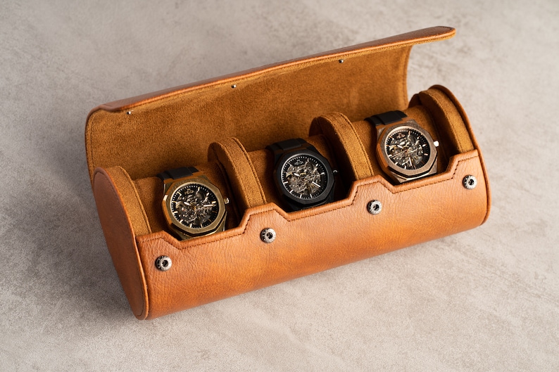 May include: A brown leather watch roll with four slots for watches. The roll is open and four watches are visible. The watches have black, gold, and silver bands and faces.