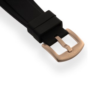 May include: Close-up of a black rubber watch strap with a rose gold buckle. The buckle has the word "WENGER" engraved on it.